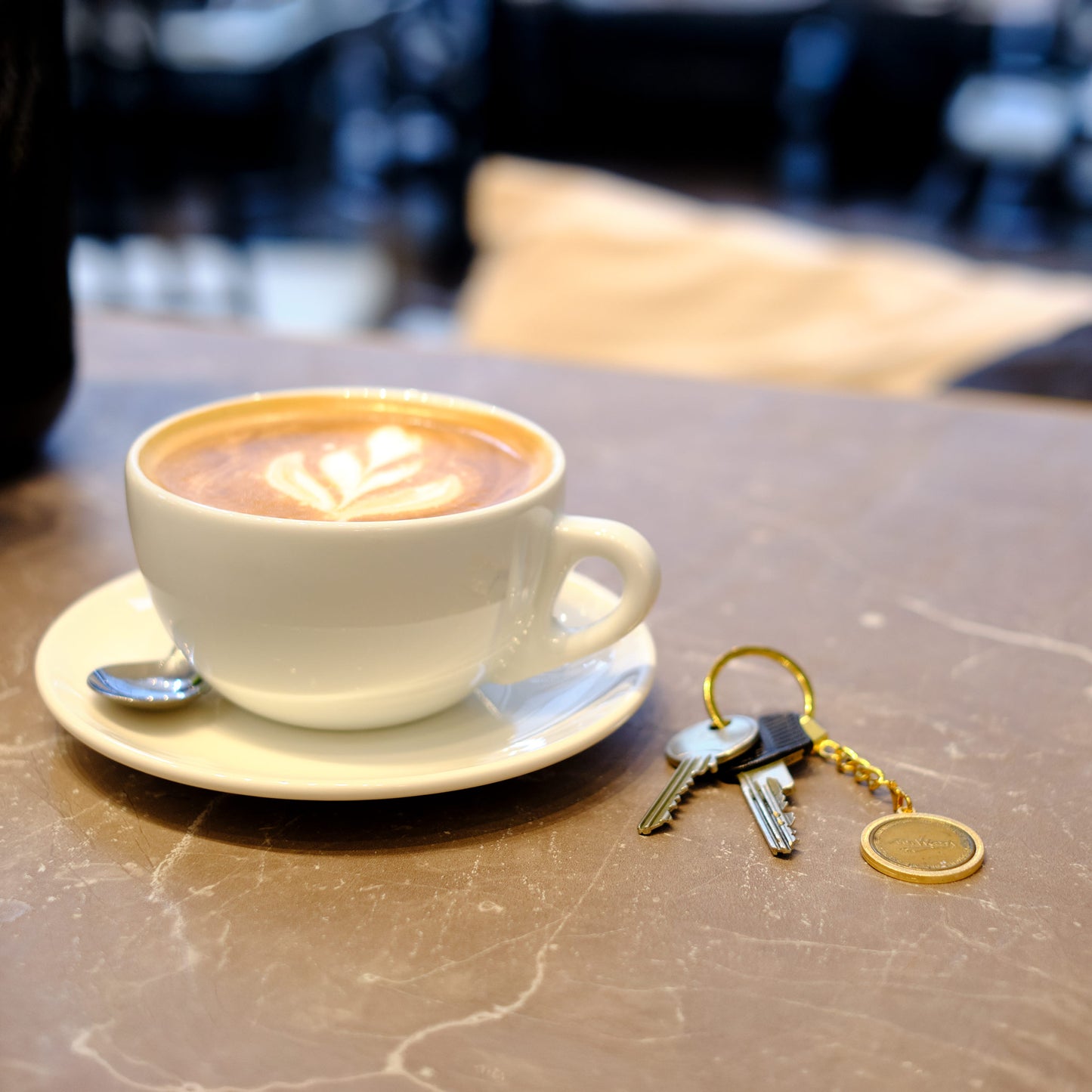 Schlüsselanhänger - Heritage - goldfarben - Freimünze Nr. 1  auf Cafetisch neben einer Tasse Cappuccino